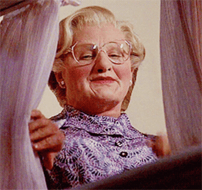An Older Woman Wearing Glasses And A Purple Shirt Is Looking Out A Window GIF