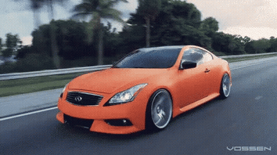 An Orange Car Is Driving Down A Road With The Word Vossen On The Bottom Right GIF