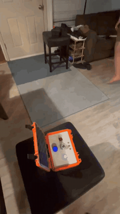 An Orange Case With A Tablet Inside Of It Sits On A Black Ottoman In A Living Room GIF