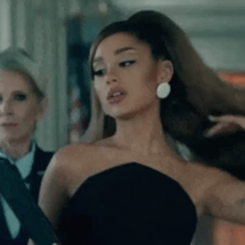 Ariana Grande Is Wearing A Black Strapless Dress And Earrings While Standing Next To A Woman . GIF
