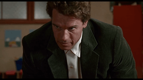 Arnold Schwarzenegger In A Suit And White Shirt Looks At The Camera GIF