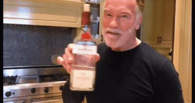 Arnold Schwarzenegger Is Holding A Bottle Of Vodka In His Hand GIF