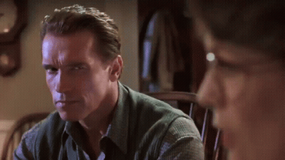 Arnold Schwarzenegger Is Sitting In A Chair With A Clock In The Background . GIF