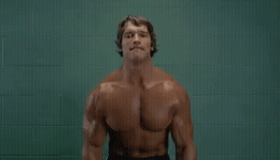 Arnold Schwarzenegger Lifting Dumbbells In Front Of Green Wall GIF