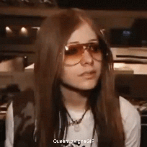 Avril Lavigne Is Wearing Sunglasses And A White Shirt While Making A Funny Face . GIF