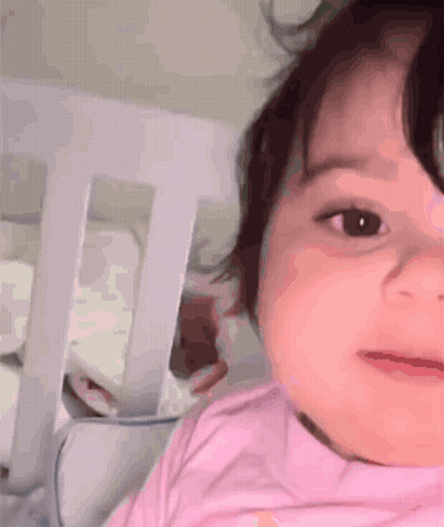 Baby Girl In Pink Shirt Laying In Crib Looking At Camera GIF