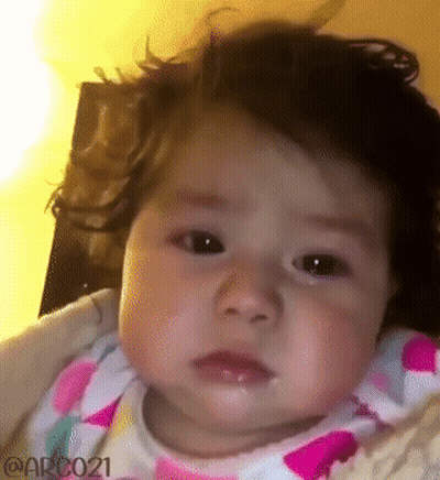 Baby Girl With Curly Hair Making Funny Face In High Chair GIF