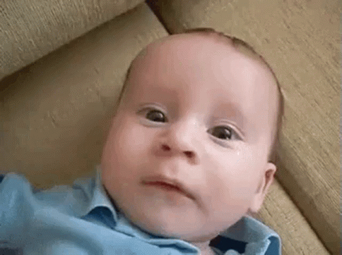 Baby In Blue Shirt Laying On Couch Making Funny Face GIF