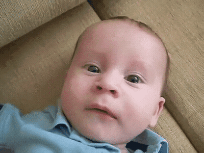 Baby In Blue Shirt On Couch Making Funny Face GIF