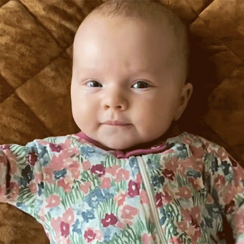 Baby In Floral Outfit Laying On Bed GIF