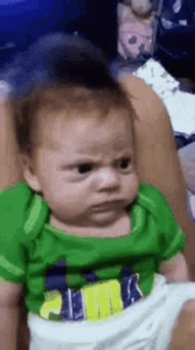 Baby In Green Shirt Making Angry Face In Chair GIF