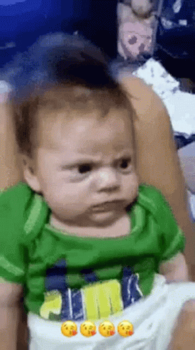Baby In Green Shirt Making Funny Face On Bed GIF