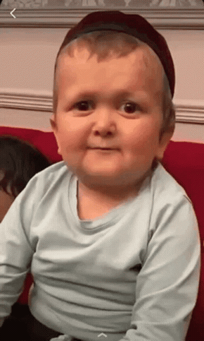 Baby In Hat And Blue Shirt Sitting On Couch GIF