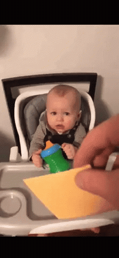 Baby In High Chair Holding Cup And Paper GIF