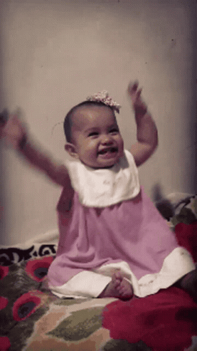 Baby In Pink Dress Sitting On Bed GIF