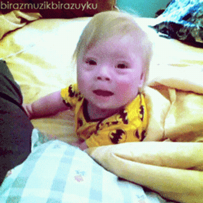 Baby In Yellow Shirt Laying On Bed GIF