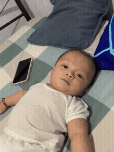 Baby Lying On Bed Next To Cellphone GIF