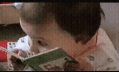 Baby Reading Book With Spoon In Mouth GIF