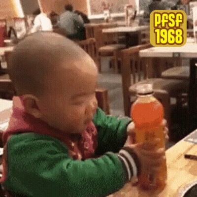 Baby Sitting At Table Holding Orange Soda GIF