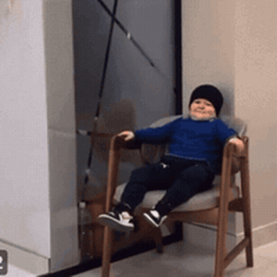 Baby Sitting In Chair Wearing Black Hat GIF