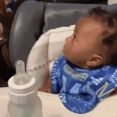 Baby Sitting In High Chair With Bib And Bottle GIF