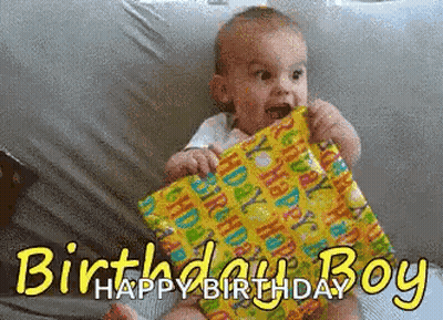 Baby Sitting On Bed Holding Birthday Present Says Happy Birthday GIF