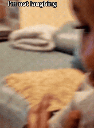 Baby Sitting On Bed Saying I'm Not Laughing GIF
