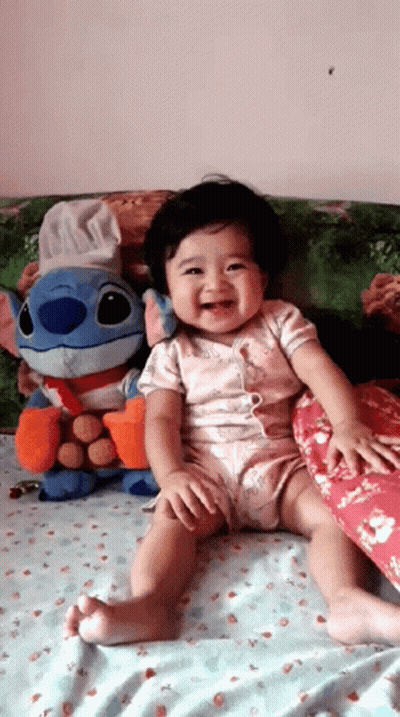 Baby Sitting On Bed With Stitch Stuffed Animal GIF