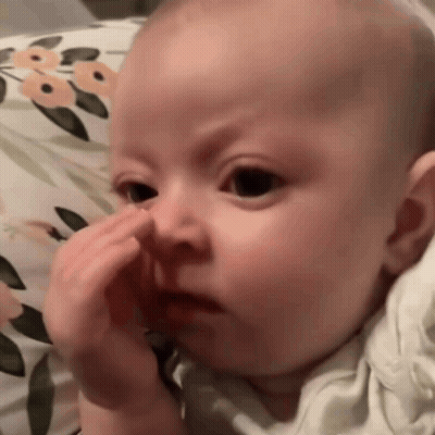 Baby Sitting On Floral Pillow Holding Nose GIF