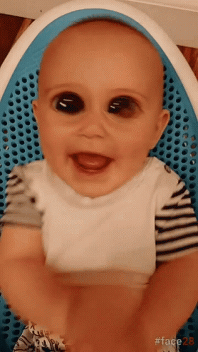 Baby With Big Black Eyes Sitting In Blue Chair Smiling GIF