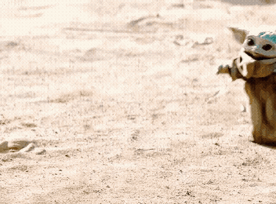 Baby Yoda Sitting On Sandy Beach Next To Person GIF