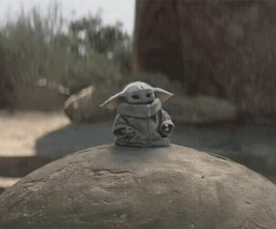 Baby Yoda Toy Sitting On Large Rock GIF