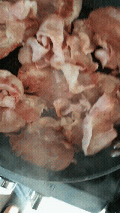 Bacon Is Being Cooked In A Pan With A Knife GIF