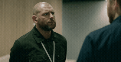 Bald Bearded Man With Lanyard Talking To Another Man GIF