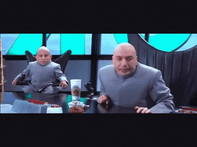Bald Man At Table With Smaller Man In Chair GIF