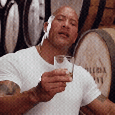 Bald Man Holding Whiskey In Front Of Barrels GIF
