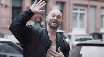 Bald Man In Black Jacket Waving And Smiling GIF