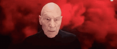 Bald Man In Black Shirt Looking At Camera GIF