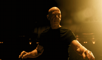 Bald Man In Black Shirt Standing In Dark Room GIF