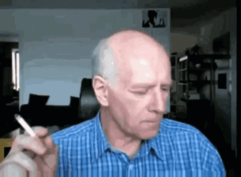 Bald Man In Blue Plaid Shirt Smoking Cigarette In Living Room GIF