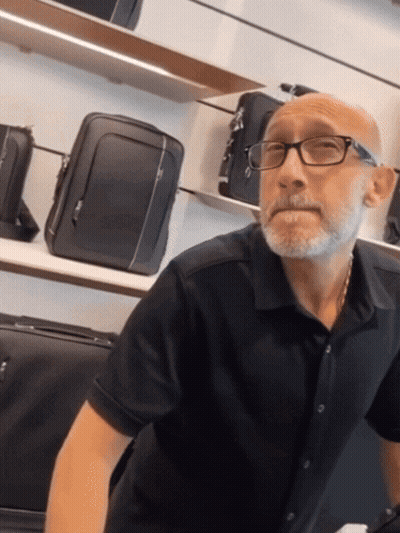 Bald Man In Glasses And Black Shirt In Front Of Suitcases GIF