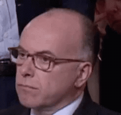 Bald Man In Glasses And Suit Sitting In Crowd GIF
