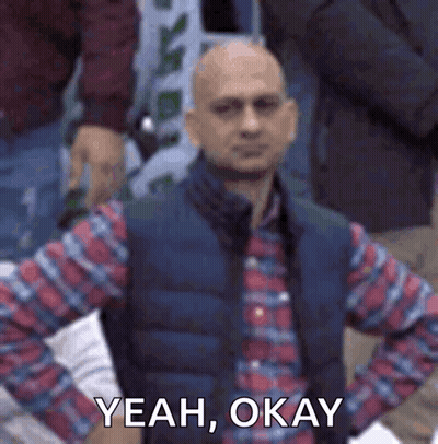 Bald Man In Plaid Shirt And Vest Sitting In Crowd GIF