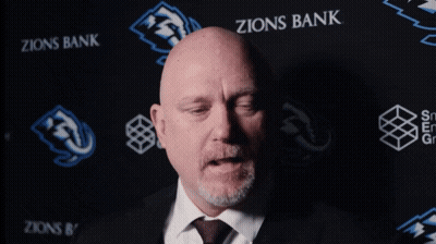 Bald Man In Suit And Tie In Front Of Zions Bank Banner GIF