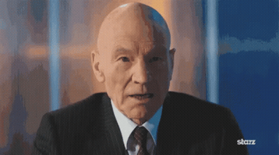 Bald Man In Suit And Tie Sitting In Front Of Blue Wall GIF