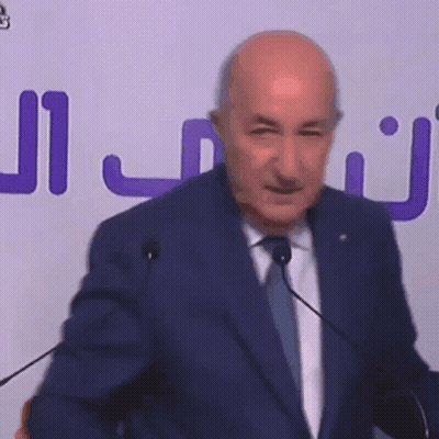 Bald Man in Suit and Tie Speaking at Microphones