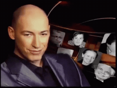Bald Man In Suit Smiling In Front Of Pictures GIF