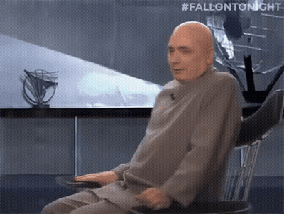 Bald Man Sitting With Hands On Hips Behind #FallonTonight Sign GIF