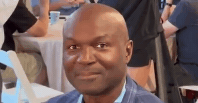 Bald Man Smiling At Table In Crowd GIF