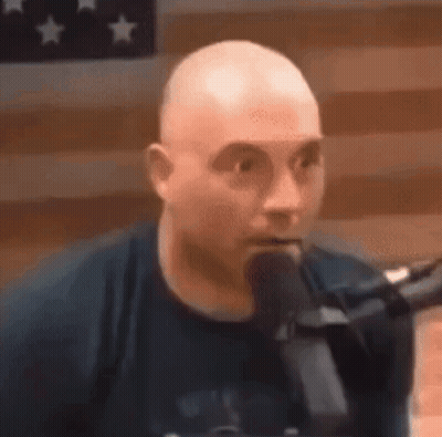 Bald Man Speaking Into Microphone Before American Flag GIF